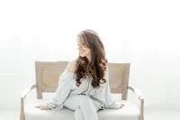 Light filled photo of a woman sitting on a bench in a Dallas TX photography studio as she looks down and smiles.
