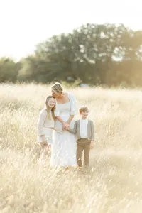 A mother and 2 children holding hands as they walk though a field at a local Dallas park.