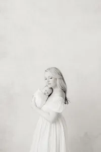 Black and white newborn portrait of a mother standing in a DFW photography studio while she holds her newborn baby girl to her chest.