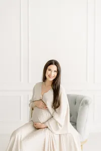 A beautiful portrait of a pregnant Dallas mother sitting on a chair holding her belly as she poses for her maternity session at a Dallas photography studio.