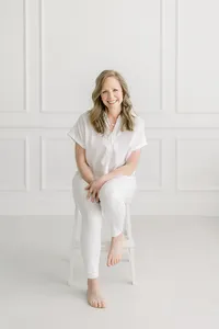 Photo taken in a photography studio of a Dallas TX business woman sitting on a chair while she leans over to pose and smile at the photographer for her professional headshots.