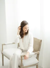 Professional headshot photo of a local Dallas business as she sits on a bench holding her hair away from her face and looking down as she smiles.
