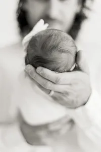 Close up black and white detail show of a dad holding her newborn baby girl.