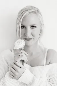 Black and white close up photo of a woman holding a fresh flower close to her face as her hair is falling in front of her face while she poses for her boudoir photos.