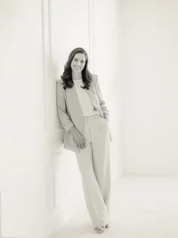 Black and white professional headshot of a Dallas TX business woman posing against a wall inside of a photography studio as she smiles while looking at the photographer.