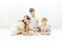 3 young siblings playing on the floor of a photography studio with wooden blocks.