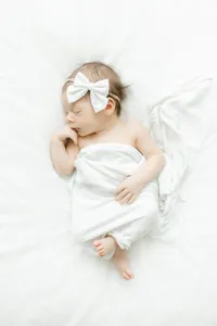 A newborn baby girl laying down on a bed for her in studio newborn session as she is wrapped loosely in a blanket while she sleeps.