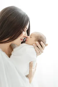 Close up photo taken as a side profile of a mother standing in a Dallas photography studio holding her newborn baby boy up as they touch noses.