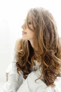 A photo of a woman sitting on a chair in a DFW photography studio as she poses for her boudoir session with her long and beautiful brown curly hair falls down her arms.