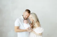 In studio newborn portrait of a mother and father holding their newborn baby girl close.