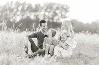 Black and white photo of a family sitting in the middle of an open field at a Dallas/Fort Worth park taking their new family photos together.