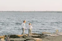 Two young brothers playing on the rocks by a lake.