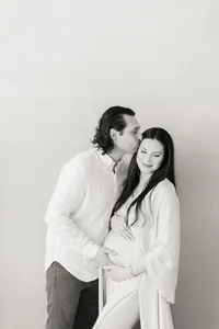 Black and white in studio maternity portrait of an expecting Dallas mother being held and kissed by her spouse.