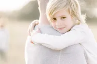 Close up photo of a boy hugging his dad and looking at his family photographer.
