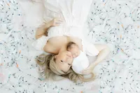 A mother laying down in a Dallas photography studio with her newborn baby girl by her side as they are surrounded by all of the needles she used during her IVF journey to have her miracle baby.
