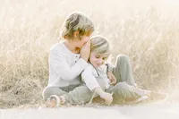Two brothers sitting in a grassy Dallas field as the big brother whispers a secret to his little brother.
