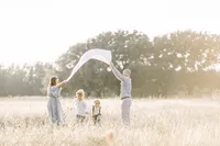 A family photo of mom an dad holding a blanket up in the air as their boys run under in the middle of a Dallas/Frisco TX field.