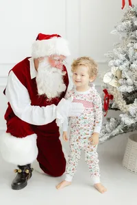 Santa holding a baby boy as they pose in front of a christmas tree