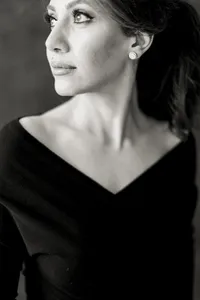A black and white photo of a woman posing for boudoir photos in a studio as she wears a black off the shoulder gown and looks over her shoulder elegantly.