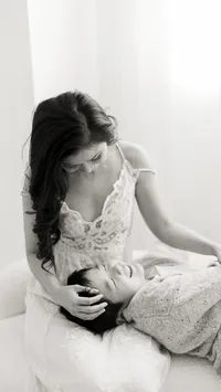 Black and white portrait of a mother sitting on the edge of a bed as her son lays on her lap while she holds him.