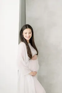 Photo of an expecting Dallas mom leaning on a wall while she is dressed in a tulle maternity gown holding her belly in a Dallas photography studio.