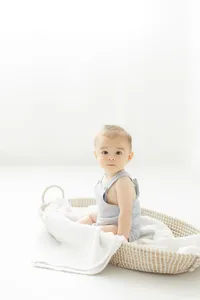 A cute little baby boy sitting in a basket in a photography studio by a window.