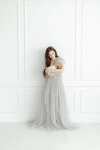 Photo of a mother standing in a Dallas photography studio while she holds her newborn baby girl close to her as she poses by a wall wearing a tulle gown.
