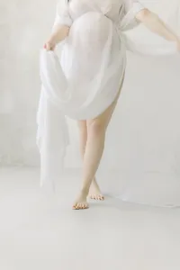 A portrait maternity session taken in a Dallas/Fort Worth area photography studio of an expecting mother from the chest down while she is dancing playfully in the studio.