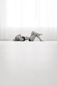 A beautiful black and white photo of a woman laying in a light filled Dallas/Fort Worth photography studio floor wearing a matching black lace lingerie set while she poses elegantly and holds her hair.