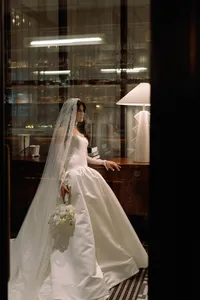 Bride in a satin gown and long veil standing by a lamp inside a luxury Huntsville hotel suite.