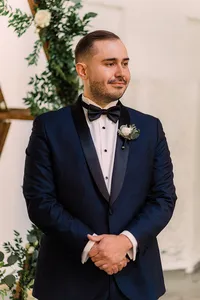 Groom stands at the altar in a sharp navy tuxedo, hands clasped and expression serene, awaiting his bride with anticipation.