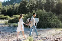 The couple holds hands while walking near a brown and white horse grazing in the background, surrounded by dense greenery.