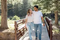 The couple walks arm in arm across a bridge, sharing a joyful moment, both dressed casually in white tops and jeans.