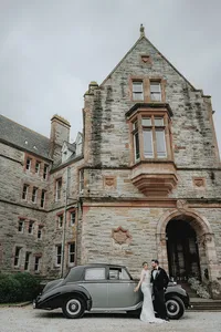 Bride and groom leaning against old car in front of Ireland castle