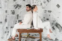 A couple sits back to back in front of newspapers