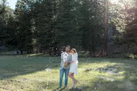 A joyful moment of the couple standing together in a grassy field as champagne bursts from a bottle, creating a celebratory spray.