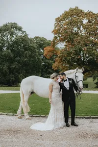 Bride looking at groom holding the reigns of a white horse