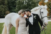 Bride and groom forehead to forehead in front of a white horse