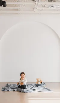 A little boy sits in front of a white wall.