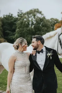 Bride and groom smiling at each other with white horse in back