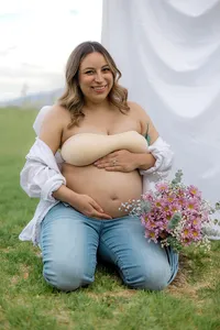 A pregnant woman sits on the ground with flowers