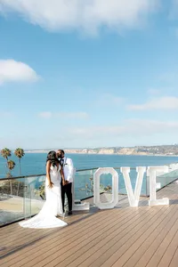 Bride and groom kissing next to "LOVE" sign with ocean in the background
