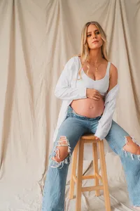 A pregnant woman poses on a stool with jeans