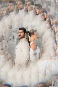 A couple stands back to back in front of newspapers