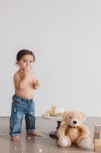 A little boy sits next to cake and a teddy bear.