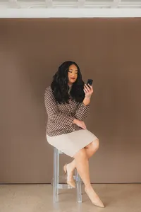 A woman seated on a stool, intently gazing at her phone