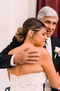 Bride, with an emotional expression, embraces her father in a heartfelt hug on her wedding day.