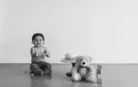 A little boy sits next to cake and a teddy bear.