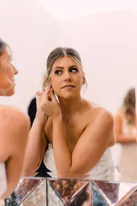 Bride adjusts her earring, looking thoughtfully into a mirror as she prepares for her big day.
