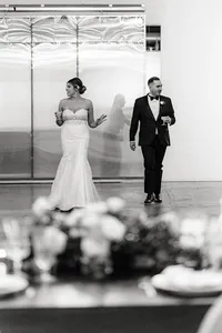In a black-and-white shot, the bride and groom are seen dancing, with the bride holding a drink and smiling. They both look relaxed, enjoying a moment together on the dance floor.